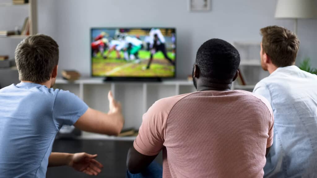 Male friends gather to watch football on a big screen TV
