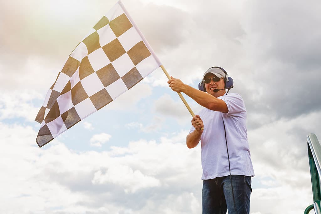 Man waves a checkered flag at the finish line of the race