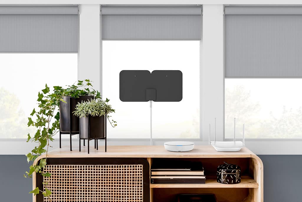 Tablo device on wicker credenza near Wi-Fi router with black TV antenna in the window behind it