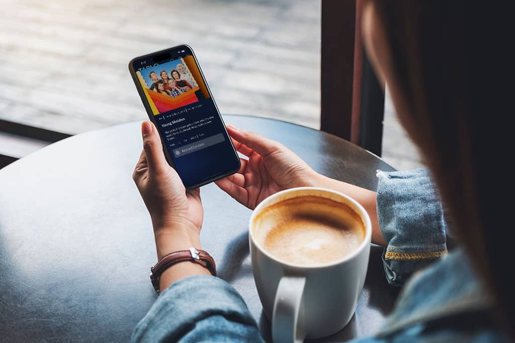 woman in a cafe using the Tablo app on her smartphone to schedule a recording