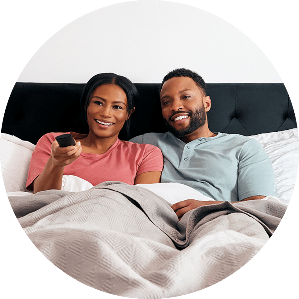 Couple cuddled in bed watching Tablo on their streaming device connected to their TV