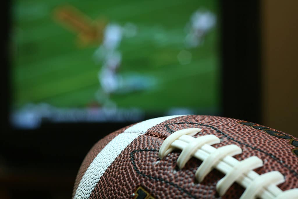 Closeup of a football in front of a television showing a football game being played